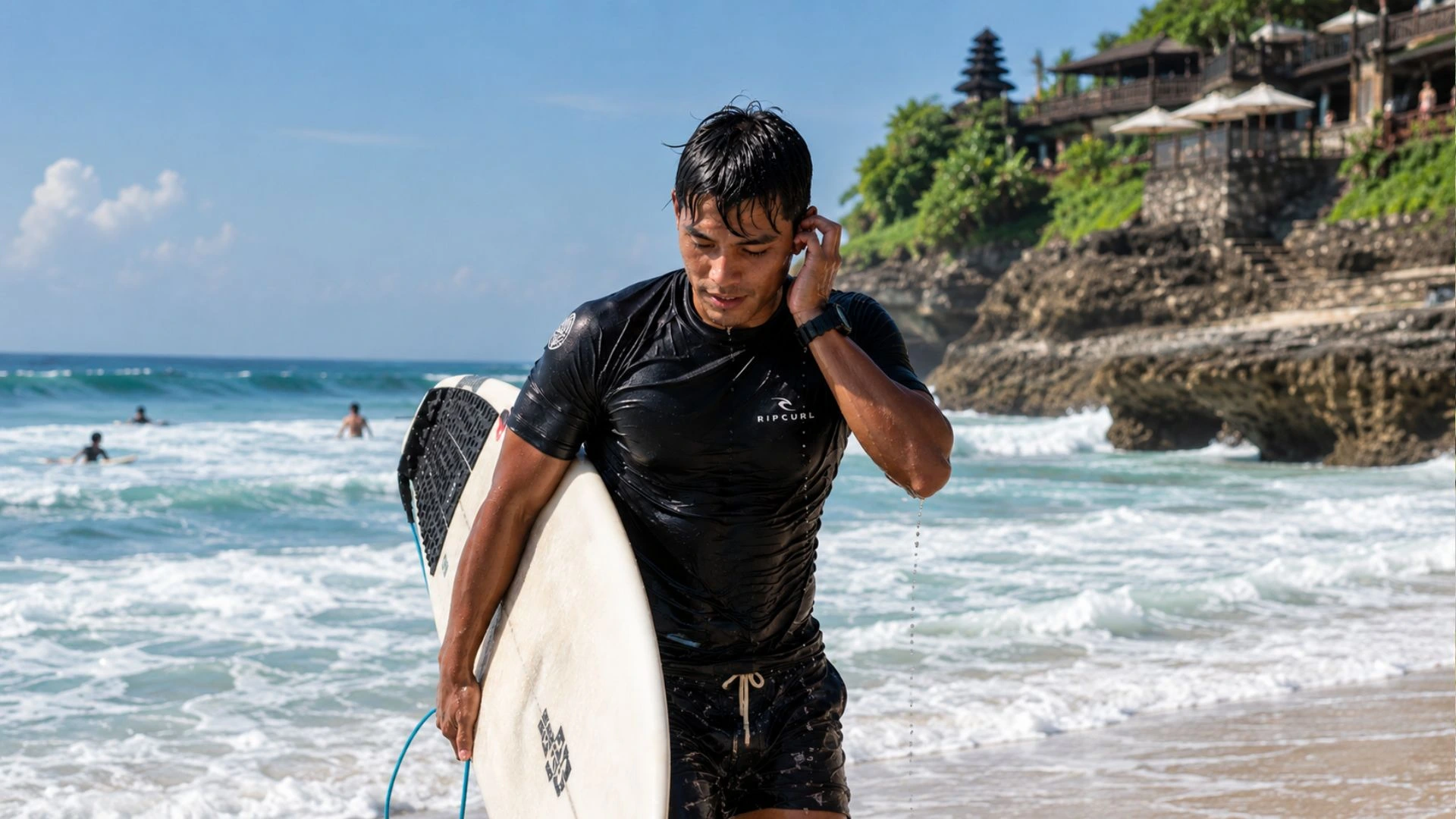 Surfer coming out of the ocean at Uluwatu Bali holding ear after water session